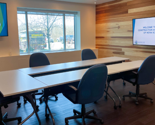 A sunny room with wood panelled walls. The room is set up for a small meeting with displays airing a powerpoint presentation which says, 'Welcome to the Construction Association of Nova Scotia"