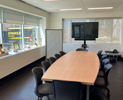 A bright board room with windows stretching across two walls. A boardroom table sits in the middle of the space with digital displays and flip chart ready to be used.