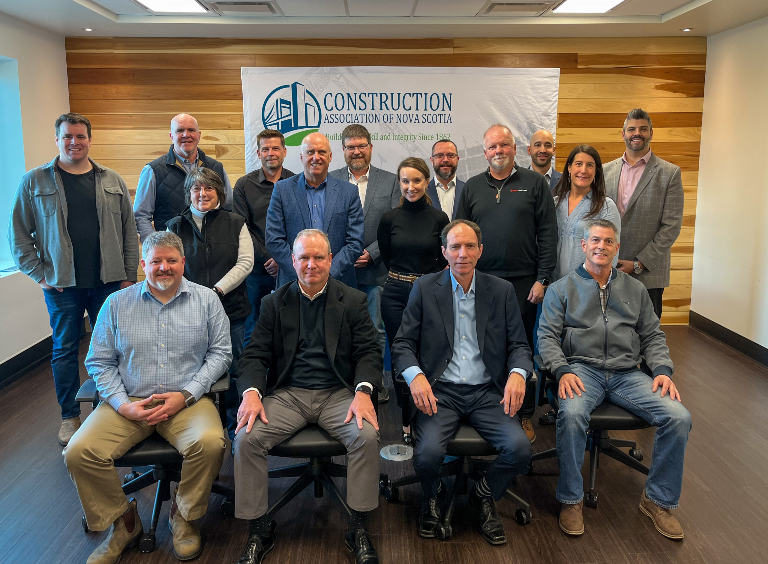 Images depicts CANS 2022-2023 board of directors. Sixteen smiling professionals stand posed in three rows. They are arranged in front of a wood-panelled wall and banner with CANS logo depicted..