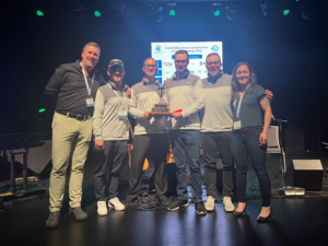 Golf Tournament winners Able Electric 2016 Limited holding a trophy on-stage.